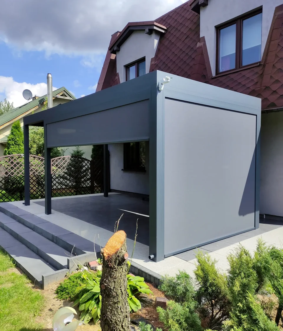Szara pergola przy domu z opuszczonymi roletami ZIP w prowadnicach bocznych