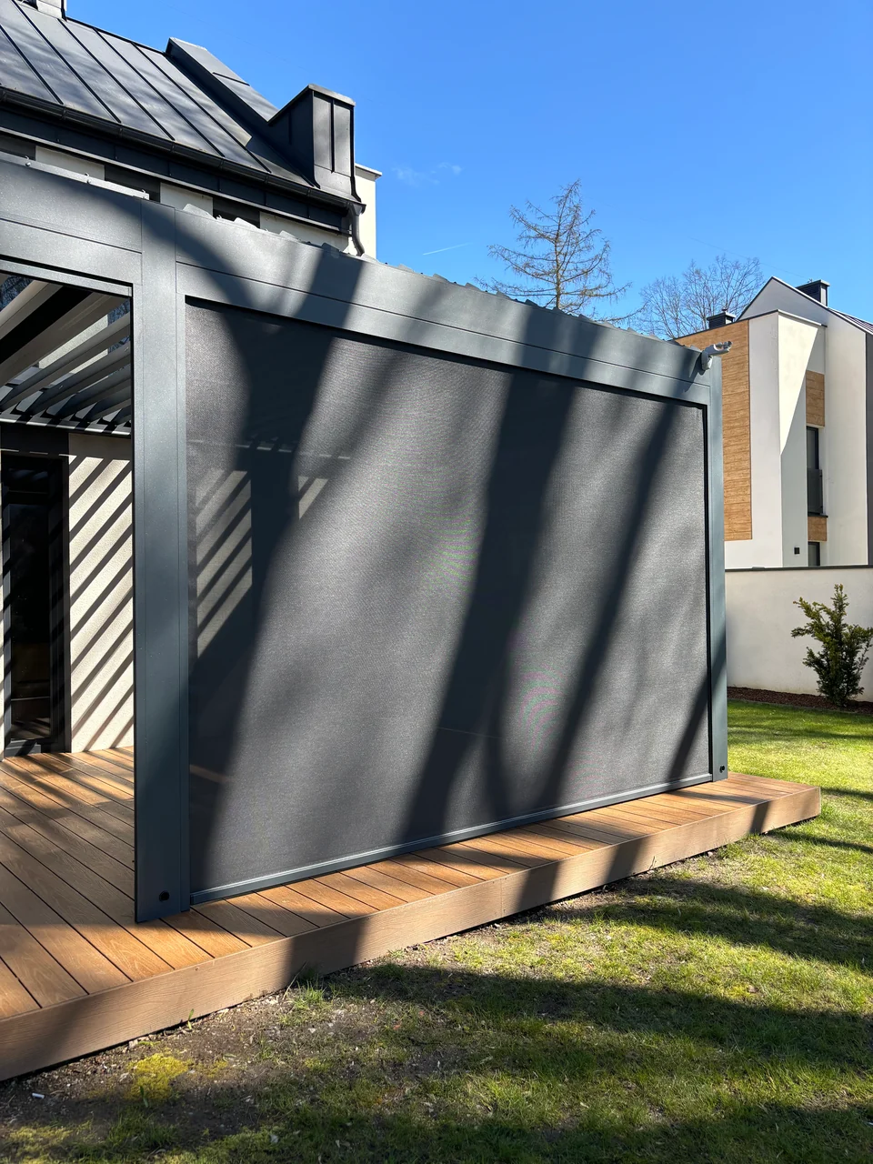 Grafitowa pergola z opuszczoną osłoną na drewnianym tarasie