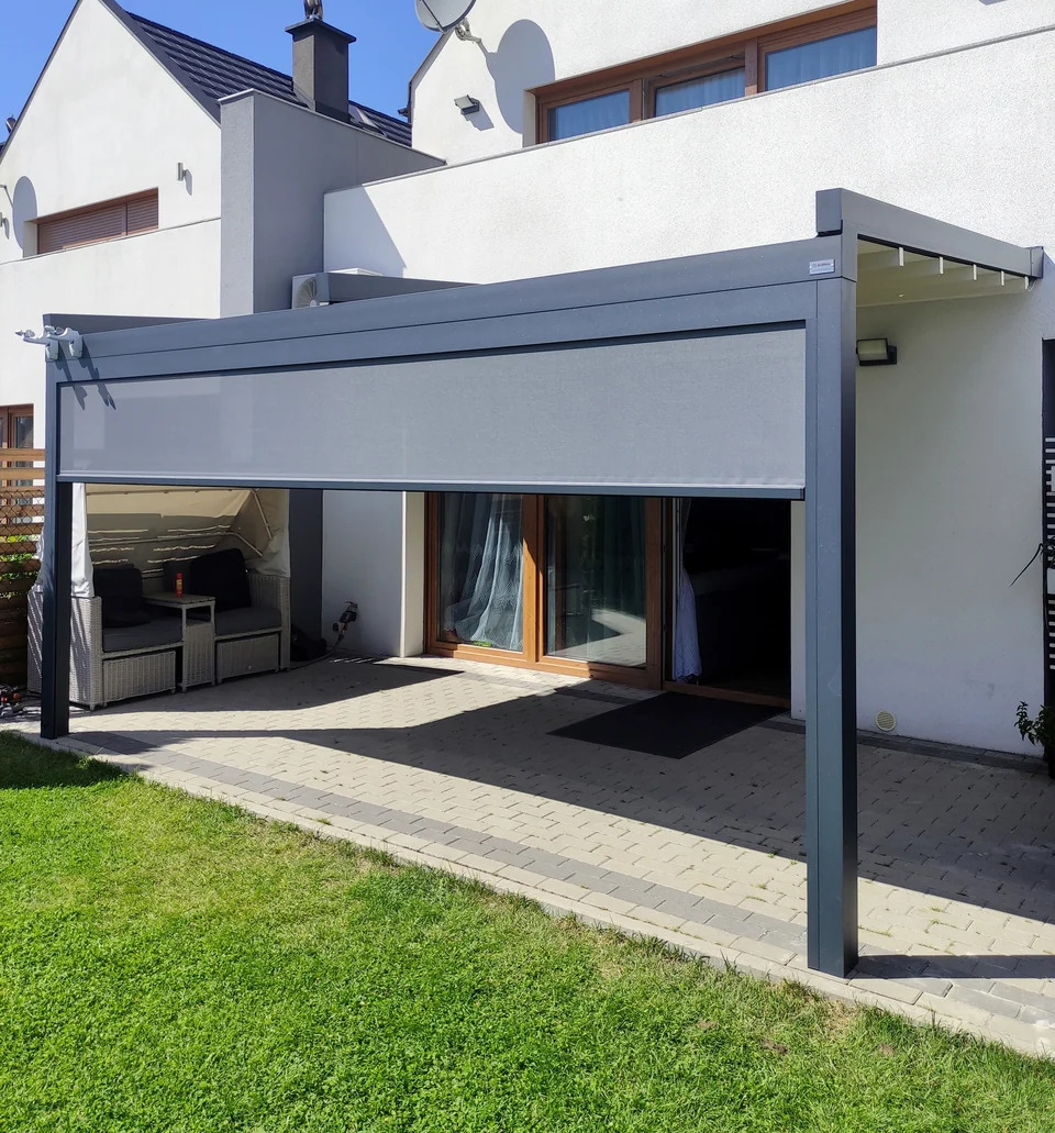 Pergola z częściowo zsuniętym jasnym dachem widziana od strony ogrodu