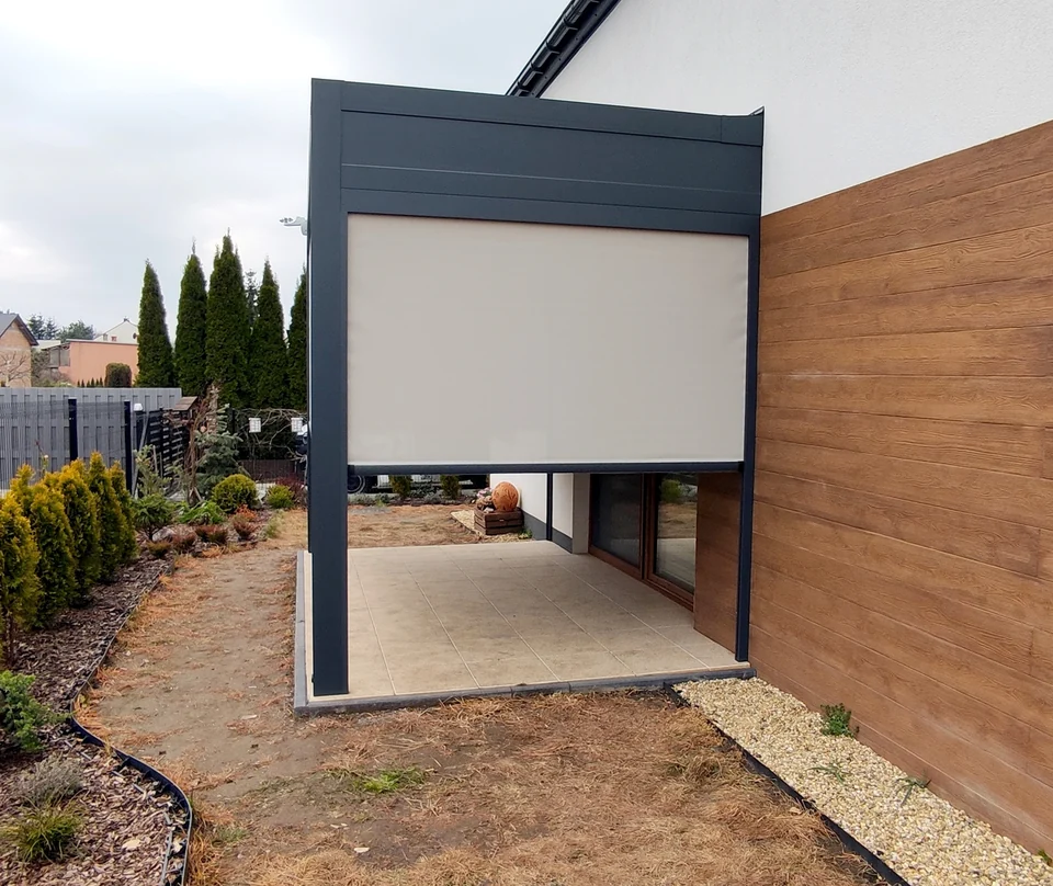 Pergola z opuszczoną jasną osłoną boczną przy drewnianym ogrodzeniu